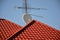 TV antennas and satellite dish for television mounted on the tiled roof of house isolated on blue sky background in countryside