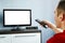 TV remote control in male hand in front of widescreen TV set with blank screen on blue wall background. Young guy switches channel