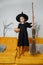 Tween age girl dressed as a witch holding a broom, posing for a photo