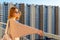 Tween redhead girl in pullover, jeans and sunglasses standing on balcony against high-rise multi-storey residential building at