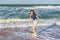 Tween slender girl standing on sand beach of sea coast against stormy waves in sunny summer day. Young woman spending summer