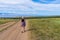 Tween tourist girl in hat and backpack walking on country road alone and admiring picturesque landscape of lake Baikal, mountains