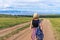 Tween tourist girl in hat and backpack walking on country road alone and admiring picturesque landscape of lake Baikal, mountains