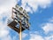 Twelve powerful spotlights on a lighting mast over the stadium against the blue sky with white clouds on a day