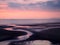 twilight view of a dark beach with a pink sky after sunset with blue clouds reflected in the water at low tide and a calm sea in
