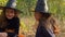 Twin girls dressed like witches are seating in a park and laughing. Closeup. 4K