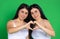 Twin girls on a green background hold hands in the shape of a heart. Love, charity, St. Valentines concept