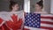 Twin sisters with Canadian and US flags watching championship on TV at home supporting hockey or football teams