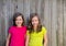 Twin sisters with different hairstyle posing on wood fence