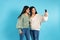 The twin sisters smile and take a selfie on a mobile phone. Blue background and empty side space