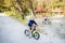 Twin toddler sibling boy and girl in autumn park, riding balance bike.