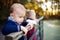 Twin toddler sibling boy and girl standing in autumn park, holding railing.