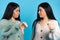 The twin women look at each other and one indicates dislike, thumb down. Photo on a blue background
