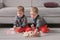 Twins boys brothers are building from wooden blocks sitting on the floor by the sofa in their room.