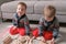 Twins boys brothers are building from wooden blocks sitting on the floor by the sofa in their room.