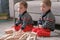 Twins boys brothers are building from wooden blocks sitting on the floor by the sofa in their room.