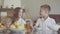 Twins brother and sister are sitting at the table in a white shirts before school and knocking with spoons, shouting