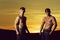 twins with strong, naked torsos posing on evening sky
