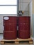 two 208 liters red metal drums on a pallet in a work area near a large door.