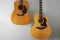 Two acoustic guitars hanging on a grey wall