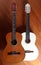 Two acoustic guitars, one light and one dark, side by side on a wooden background