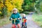 Two active brother boys driving on bikes in autumn forest