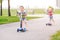 Two active little children friends girl and boy riding scooters on road in park outdoors