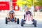 Two active little kid boys driving pedal race car in summer garden, outdoors. Children, best friends racing with fast