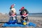 Two adorable Havanese puppies posing in Christmas outfits and hannukah toys on a blue towel on the beach at the edge of the ocean