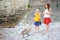 Two adorable little girls feeding young swan on a pebble beach