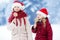 Two adorable little sisters wearing Santa hats having huge striped Christmas lollipops on beautiful winter day