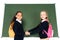 two adorable multicultural schoolgirls holding hands while standing near chalkboard isolated on white.