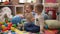 Two adorable toddlers sitting on floor sucking construction block at kindergarten