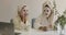 Two adult Caucasian girls with face masks sitting at the table and chatting. Positive women in hair towels and bathrobes