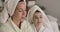 Two adult Caucasian women taking off face masks. Beautiful girls in hair towels and bathrobes resting at home. Cinema 4k