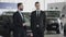 Two adult men discussing a new car in a dealership. Young dealer and a dealership client talking in a showroom.