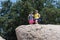 Two adult women hikers stand on the top of a giant boulder, happy, in the sunshine