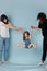 Two adults lifting little girl by hands for her amusement over blue background