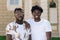 Two African American friends are standing in the street and smiling. Male portraits close up.