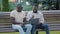 Two African American male friends or colleagues sitting on bench in city park using laptop. Black men looking at