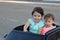 Two amazing girls ride in one big toy car on city street asphalt. Outdoor driving in a summer attraction for children