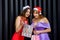 Two amazing women in santa hats and elegant evening dresses holding shopping bags