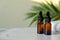 Two amber glass bottles for serum or essential oil on marble table, green palm leaf on the background. Brown dropper bottles with