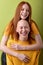 Two american redhead and bald ladies models hugging isolated over green background