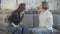 Two angry young women yelling and gesturing sitting on couch indoors. Side view portrait of irritated Caucasian friends