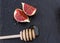Two appetizing piece of fruit figs in honey and a wooden spoon on a black background.