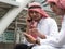 Two Arabic muslim wear white shirt humble sitting at front modern office discussing work with tablet and use the smartphone