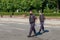 Two armed bodyguards in black uniforms, protective masks, gloves patrol city streets during global pandemic.