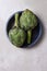 Two artichokes in a blue bowl on a mottled gray background