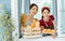 Two Asian beautiful female friends wearing aprons, standing and while opening window, welcome, happily smiling, serving breakfast